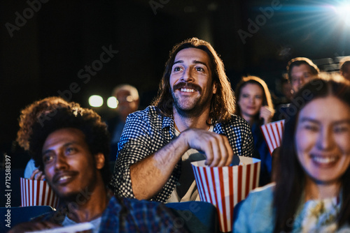 Smiling young man with popcorn watching movie in packed theater photo