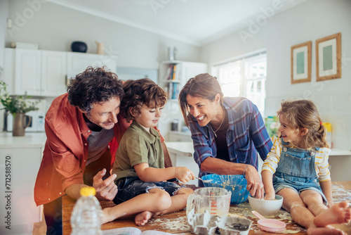 Family baking together in the kitchen with children making a mess photo