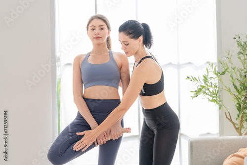 Two women confident training yoga. Athletic women in sportswear doing fitness stretching exercises at home in the living room. Sport and recreation concept. Yoga teacher is helping young woman.