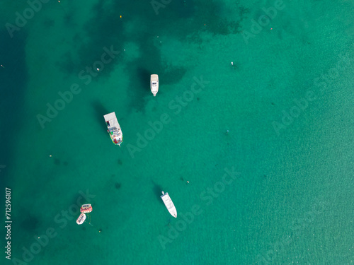 Four boats moored in calm clear turquoise sea in Malta near Mellieha aerial view top down photo