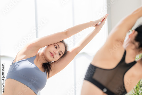 Two women confident training yoga. Athletic women in sportswear doing fitness stretching exercises at home in the living room. Sport and recreation concept. Yoga teacher is helping young woman.