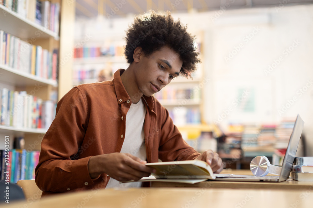 Focused African American student guy sitting at desk in university library, reading book, preparing for an exam, dedicated scene of academic focus and preparation Focused African American student guy sitting at desk in university library, reading book, preparing for an exam, dedicated scene of academic focus and preparation