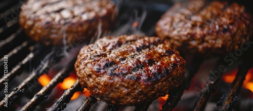 Close-up view of grilled homemade beef hamburger patties cooking on charcoal barbecue grates at a backyard cookout. photo