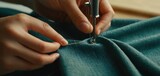  a close up of a person working on a piece of cloth with a sewing machine in the foreground and a hand holding a needle in the middle of the fabric.
