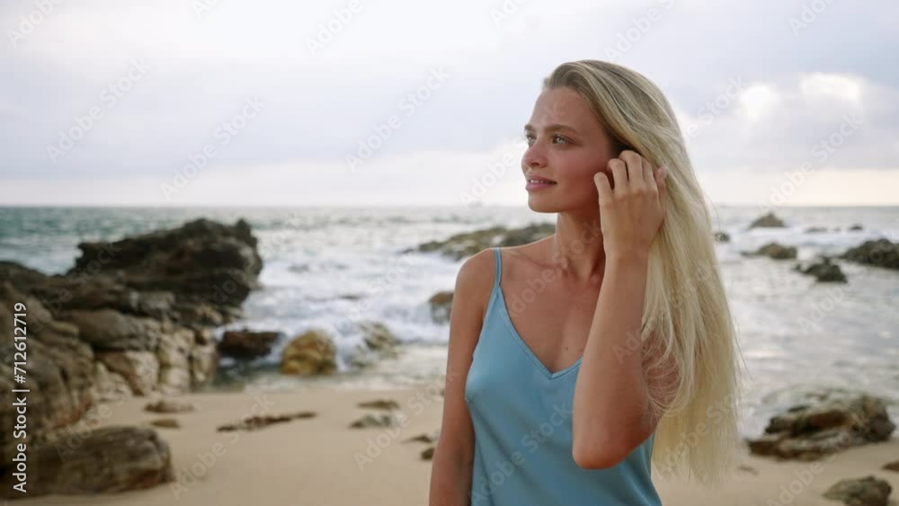 Sun-tanned woman in blue dress enjoys serene beach. Blonde hair, blue sea, stroll on sandy shore. Leisure, travel, summer concept, natural beauty, sunset vibes. Sun-tanned woman in blue dress enjoys serene beach. Blonde hair, blue sea, stroll on sandy shore. Leisure, travel, summer concept, natural beauty, sunset vibes.