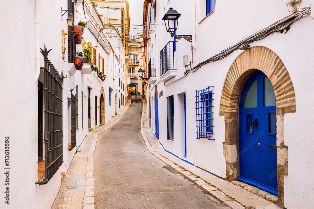 Fototapeta premium A charming narrow street lined with traditional white houses and blue accents in the coastal town of Sitges, near Barcelona.