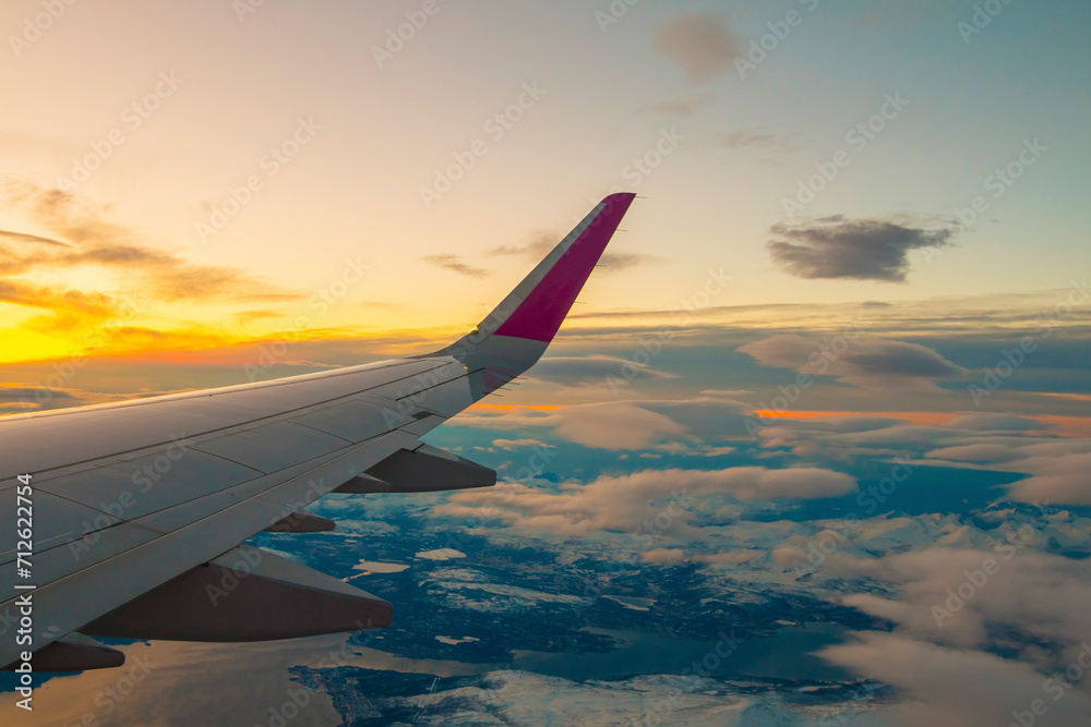 The view from the airplane window to the clouds and sunset. Airplane wing above thick pink and orange clouds. Wonderful breathtaking view.