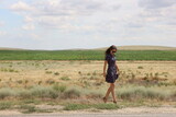 A young slender woman walking cross the field 