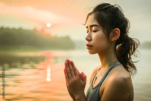 A young woman meditates peacefully by a tranquil lake at sunset, embodying serenity and mindfulness.
