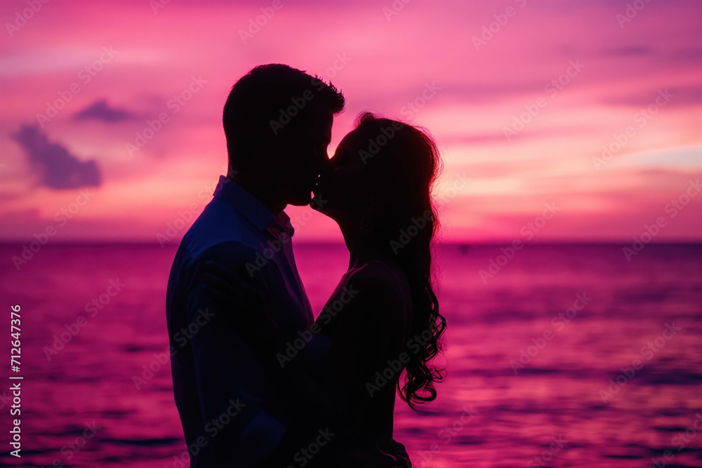 Silhouette of a young couple in love kissing on background of the pink sky during sunset.