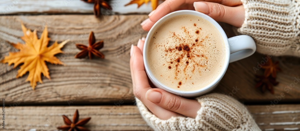 Woman's hands in knitted sweater holding coffee mug, enjoying spiced latte. Winter drink on rustic table, with spices. Top view close up. Woman's hands in knitted sweater holding coffee mug, enjoying spiced latte. Winter drink on rustic table, with spices. Top view close up.