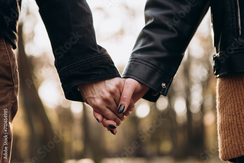 Cropped image hands young loving couple walking outside in the city park in sunny weather, hugging smiling kissing laughing spending time together. Autumn, fall season, orange yellow red maple leaves  © Volodymyr