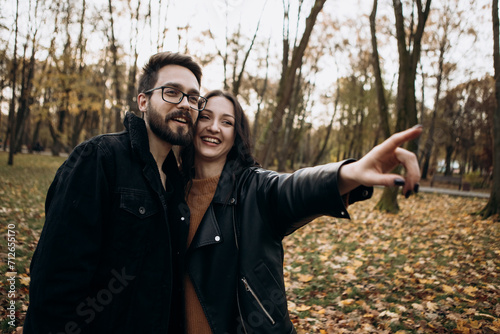 Heterosexual caucasian young loving couple, woman pointing finger at something in sunny weather, hugging smiling kissing laughing spending time together. Autumn, fall season, orange yellow red maple l © Volodymyr