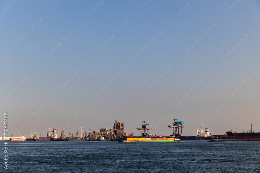 Ships float across the North Sea. Windmills in the background. Slow motion. Sea port in the Netherlands. A lot of cranes for loading goods. Different ships and barges.