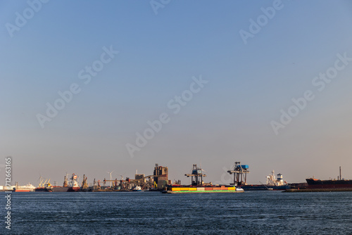 Ships float across the North Sea. Windmills in the background. Slow motion. Sea port in the Netherlands. A lot of cranes for loading goods. Different ships and barges.