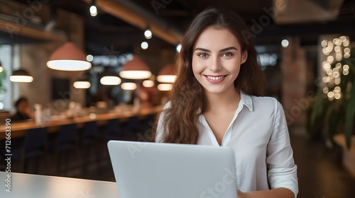 A girl in an attractive white shirt with red lipstick and a laptop, who smiles and holds a pen, is providing customer service.