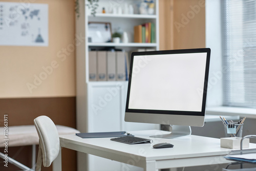 Medium shot of computer monitor with white copy space screen and stationery on table in doctors consulting room photo