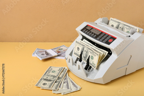 Modern cash counting machine with dollar banknotes on color background photo