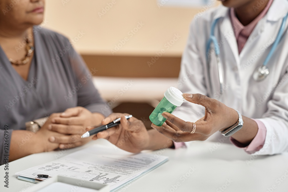 Fototapeta premium Close up shot of green plastic bottle with pills in hand of female doctor talking to patient during consultation in clinic