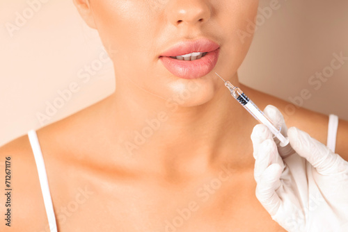 Young woman receiving lip injection on beige background  closeup