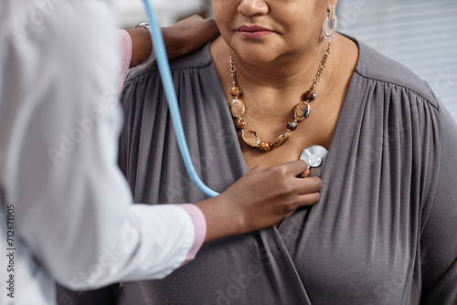 Cropped shot of unrecognizable female patient at check up in clinic with doctor pressing stethoscope to her chest photo
