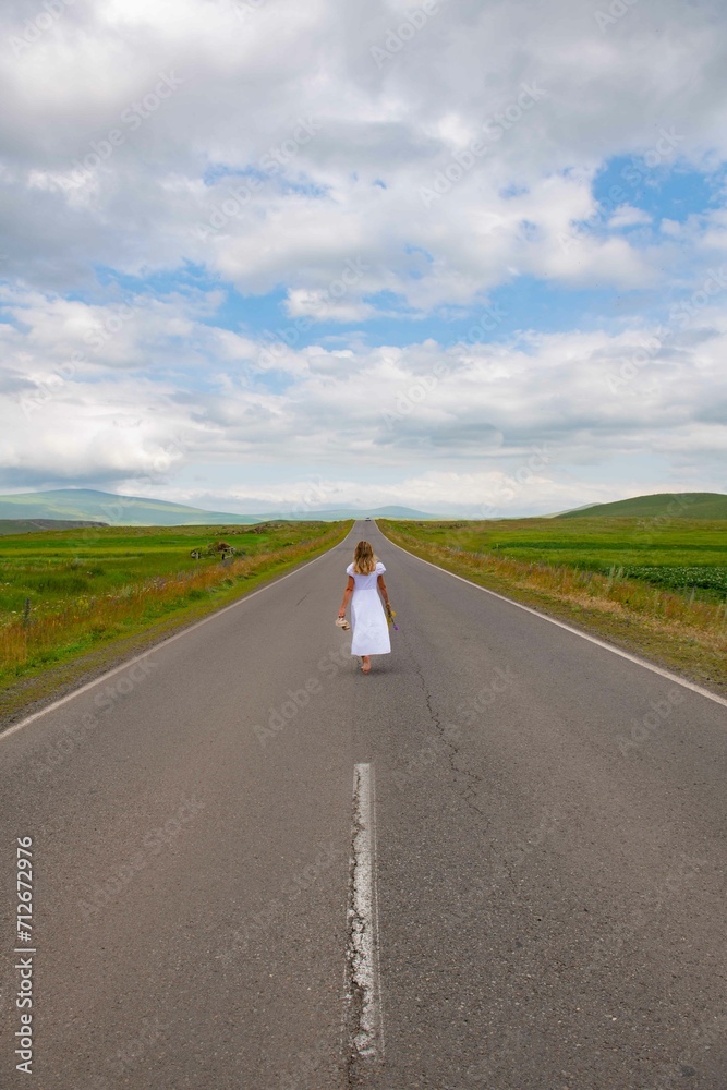 Fototapeta premium A girl in a white dress is walking along the road