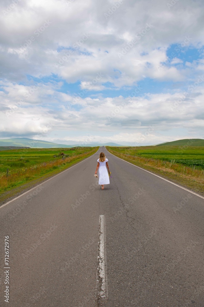 A girl in a white dress is walking along the road