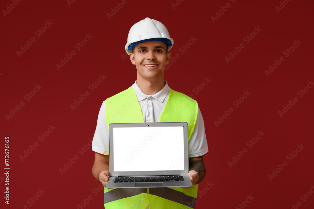 Young male engineer showing laptop with blank screen on red background Young male engineer showing laptop with blank screen on red background
