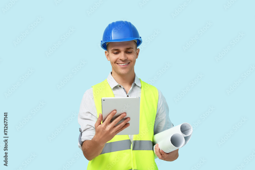 Young male engineer with blueprint and tablet computer on blue background Young male engineer with blueprint and tablet computer on blue background