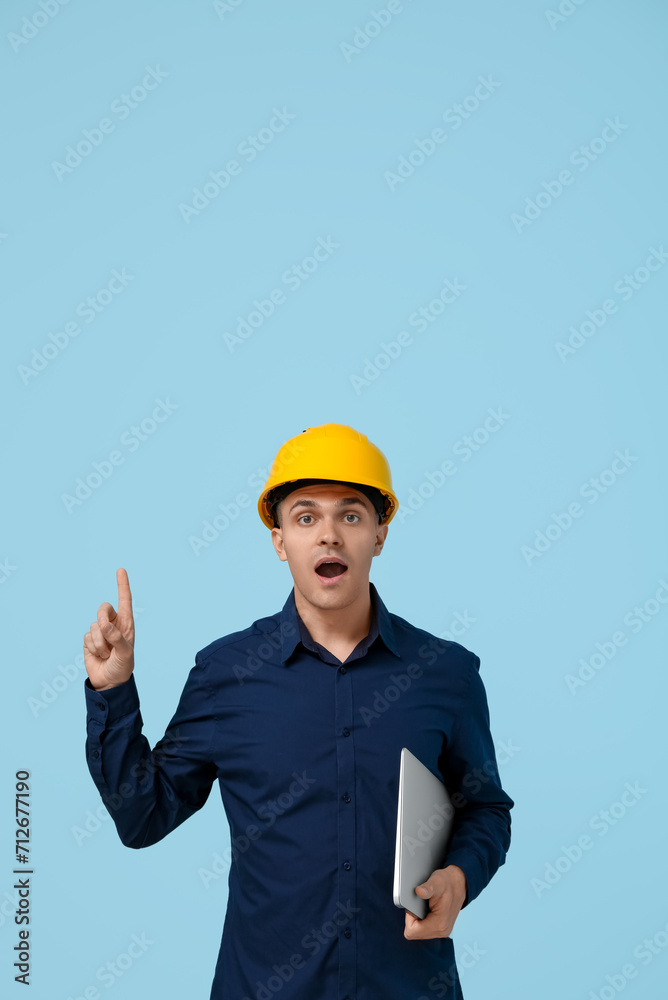 Surprised male engineer with laptop pointing up on blue background Surprised male engineer with laptop pointing up on blue background