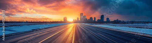 winter highway at sunset headed to a vast large city skyline. vibrant warm fiery sunset sky. winter season. snow covered landscape. sunny winter highway. cityscape at sunset. 