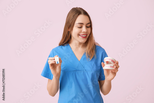 Female dentist with jaw and tooth models on pink background. World Dentist Day