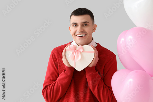 Handsome man with gift and balloons on light background. Valentine's Day celebration © Pixel-Shot