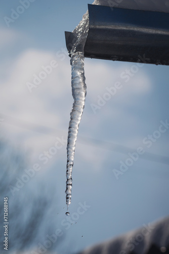 Icicles hang on the roof of a house. Winter landscape with icicles hanging from the roof of the house. Set of snow icicles, snow hat. Soft focus on ice icicle. Weather. Meteorology. 