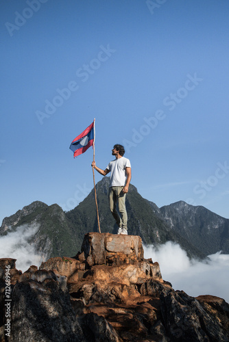 Personne qui tient un drapeau en haut d'une montagne. Randonnée et marche, arriver au sommet. Voyage au Laos, homme qui à atteint ses objectifs.