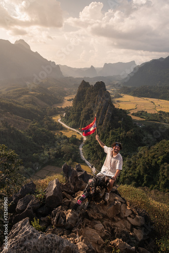 Personne en voyage assis sur une moto et qui tient un drapeau du Laos. Randonnée en haut d'une montagne, réussir à gravir le sommet. Fier d'avoir réussi, heureux d'être là. 