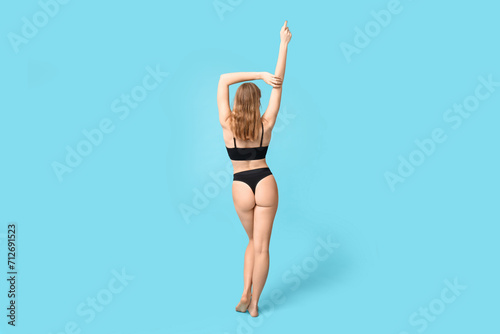 Pretty young woman in black cotton underwear on blue background, back view