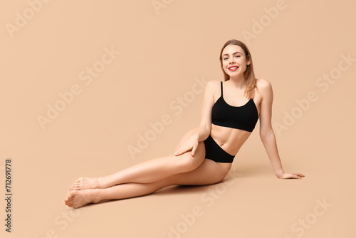Beautiful young woman in black cotton underwear sitting against beige background © Pixel-Shot