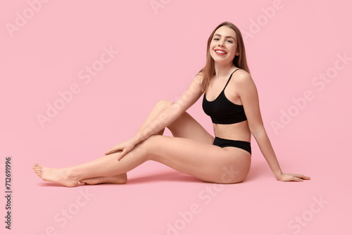 Sexy young woman in black cotton underwear sitting against pink background