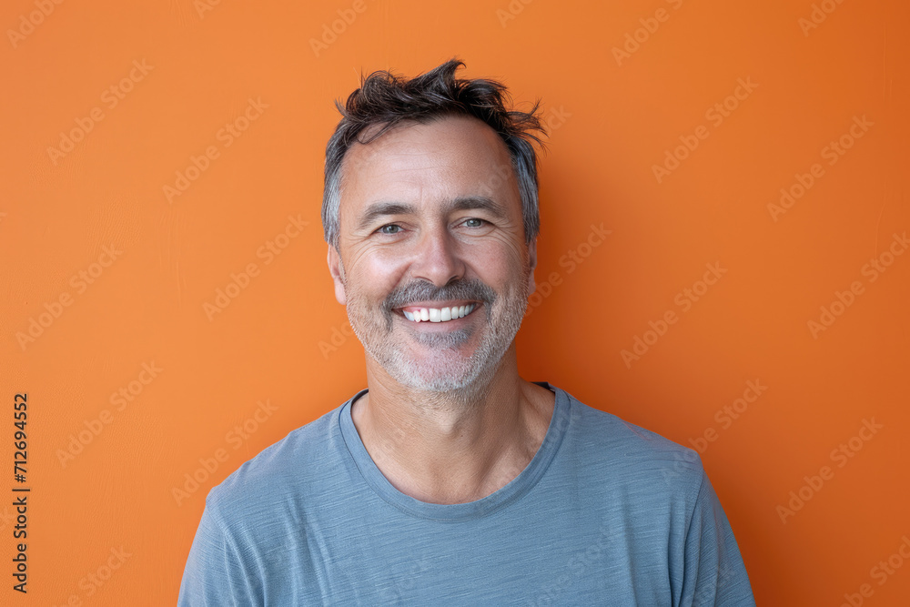 A man with a beard is smiling in front of an orange wall A man with a beard is smiling in front of an orange wall