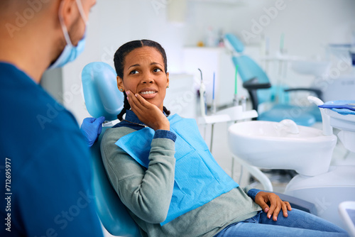 Black woman complaining about toothache during appointment at dentist's office.