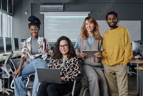 Diverse group of young programmers posing together at office holding gadgets and smiling at camera