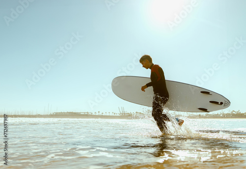Handsome male surfer in wetsuit with his surfboard entering the sea. Surfing and ocean