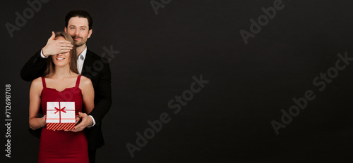 Attractive man closes his eyes and gives a gift isolated on a black background. Couple in love celebrating Valentine's Day. Wide format photo