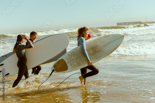 Group of friends with surfboards entering towards ocean for surfing on waves. High quality photo