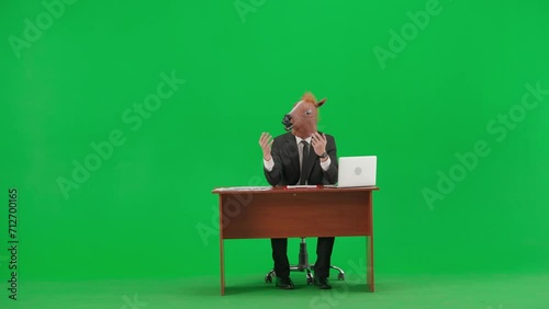 Man in business suit with horse head mask on studio green background. Businessman sits at desk, says something and points his hand to the sides. Concept of heavy office work. photo