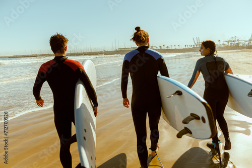 Canvas Print Back view of group of friends with surfboards in wetsuit entering towards ocean