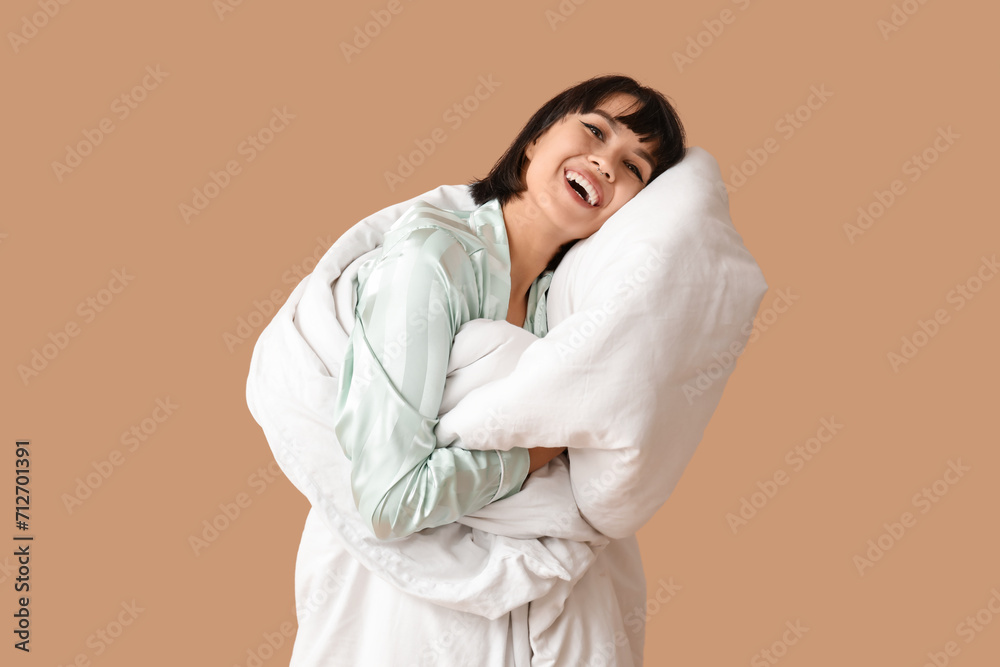Beautiful young woman in pajamas with blanket on brown background Beautiful young woman in pajamas with blanket on brown background