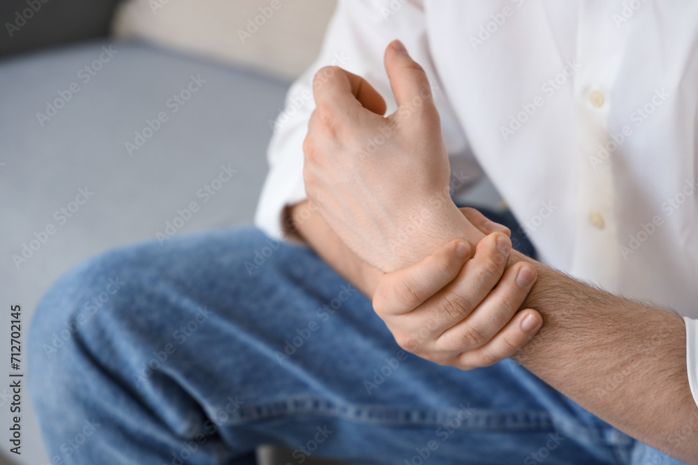 Young man suffering from wrist pain at home, closeup