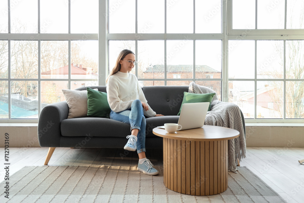Young woman sitting on sofa near window in living room Young woman sitting on sofa near window in living room